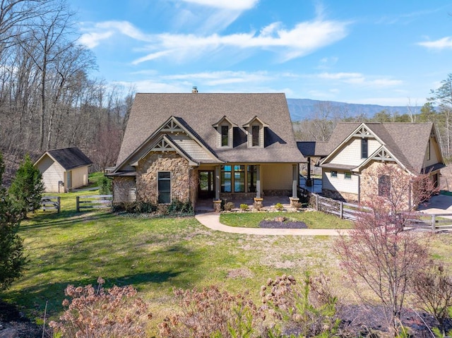 view of front of house with stone siding, a shingled roof, a front lawn, and fence