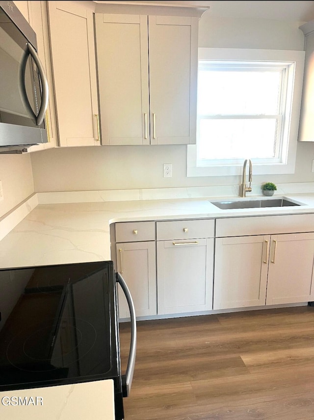 kitchen with hardwood / wood-style floors, white cabinetry, range, and sink