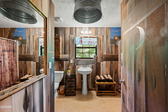 bathroom with wooden walls, sink, a textured ceiling, and toilet