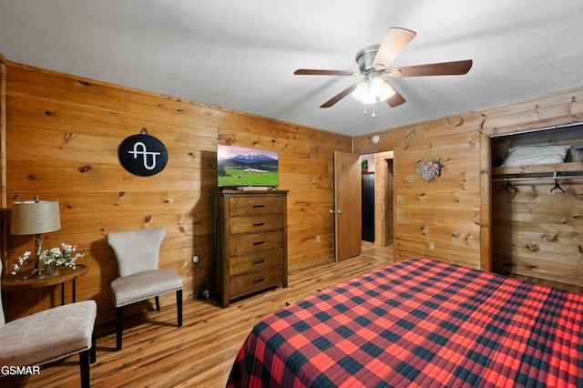 bedroom with ceiling fan, wooden walls, and light hardwood / wood-style flooring