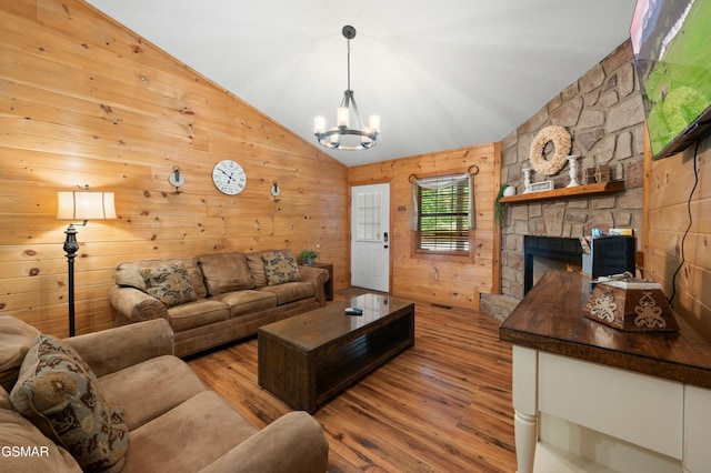 living room with a stone fireplace, wood walls, vaulted ceiling, light hardwood / wood-style flooring, and a notable chandelier