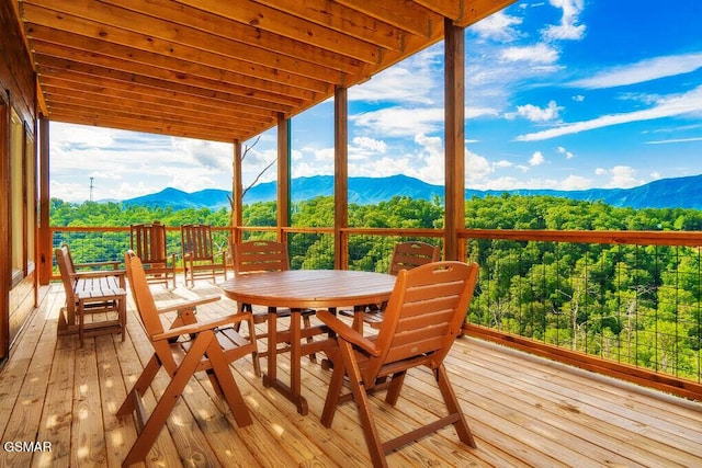 wooden terrace featuring a mountain view, a view of trees, and outdoor dining space