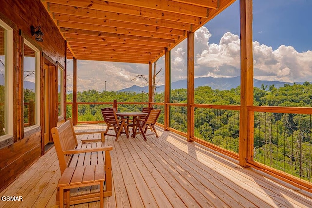 wooden deck with outdoor dining space, a wooded view, and a mountain view