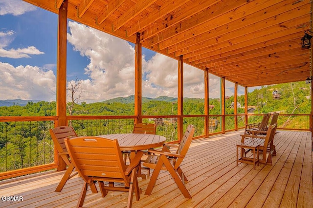 wooden terrace with a mountain view, a view of trees, and outdoor dining space