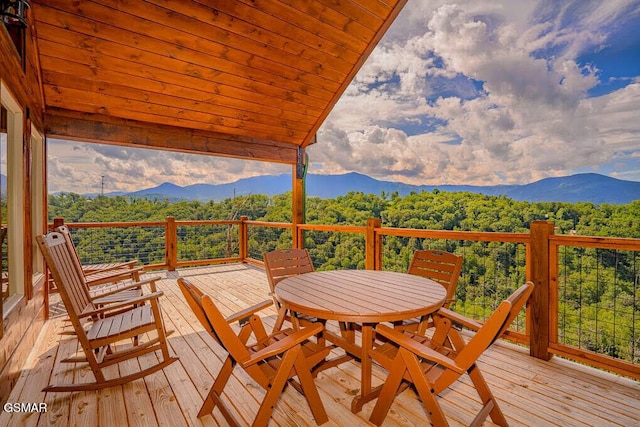 wooden deck featuring outdoor dining space, a wooded view, and a mountain view