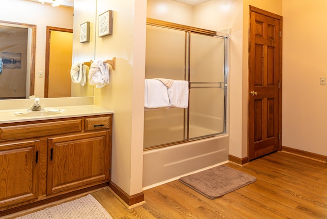 bathroom featuring wood-type flooring, vanity, and bath / shower combo with glass door