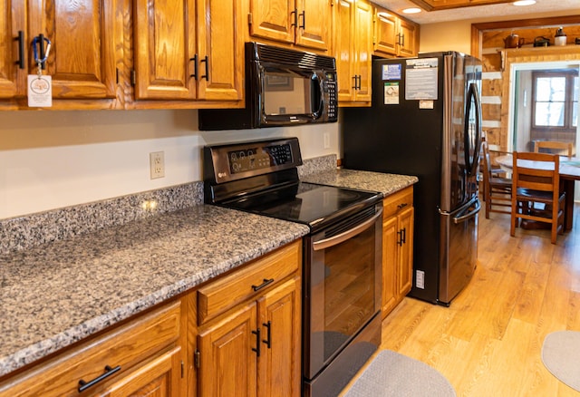 kitchen featuring black appliances, light hardwood / wood-style floors, and light stone counters