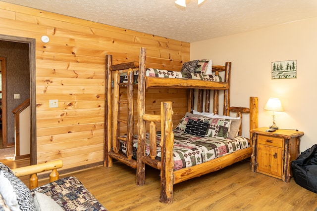 bedroom featuring a textured ceiling, light hardwood / wood-style floors, and wood walls