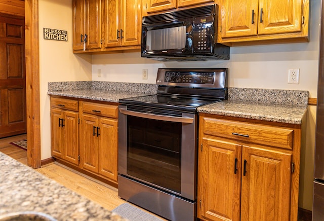 kitchen featuring light stone countertops, light wood-type flooring, and stainless steel range with electric cooktop