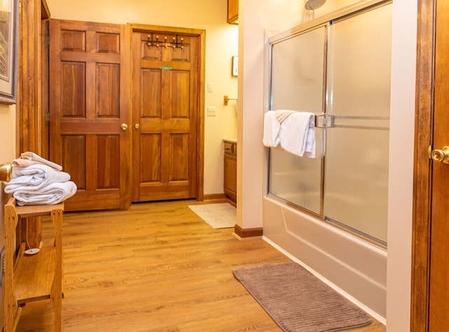 bathroom with bath / shower combo with glass door and wood-type flooring