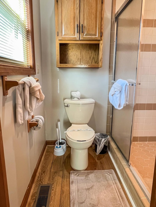 bathroom featuring wood-type flooring, toilet, and a shower with shower door