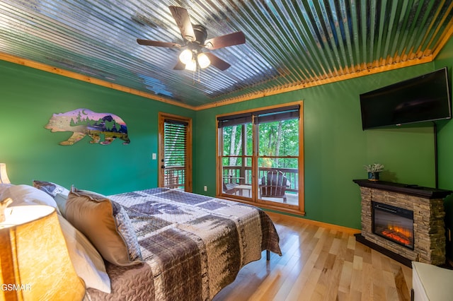 bedroom featuring ceiling fan, a stone fireplace, crown molding, and light hardwood / wood-style flooring