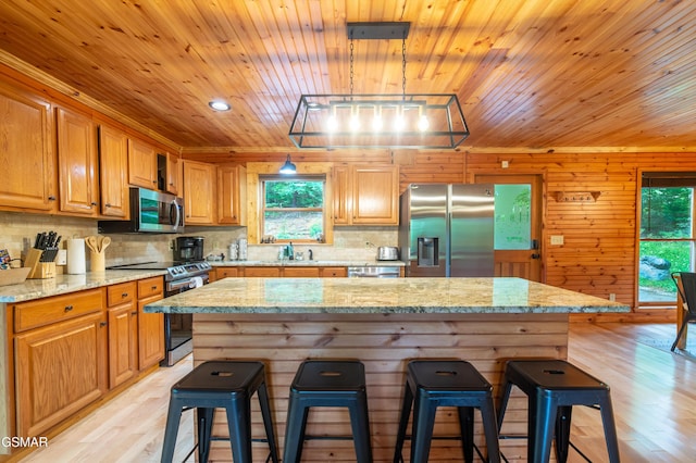 kitchen with a center island, a breakfast bar area, light stone countertops, decorative light fixtures, and stainless steel appliances