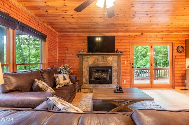 living room featuring light wood-type flooring, ceiling fan, wooden walls, wooden ceiling, and a stone fireplace