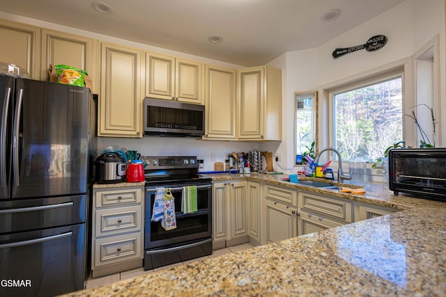 kitchen with stainless steel appliances, light stone counters, cream cabinets, and sink