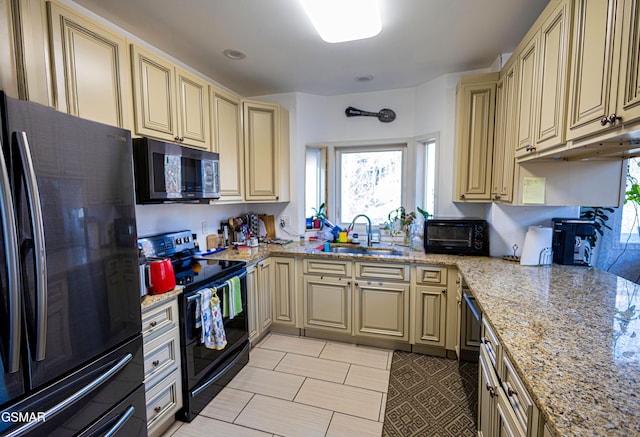 kitchen with light tile patterned flooring, black appliances, light stone counters, cream cabinets, and sink