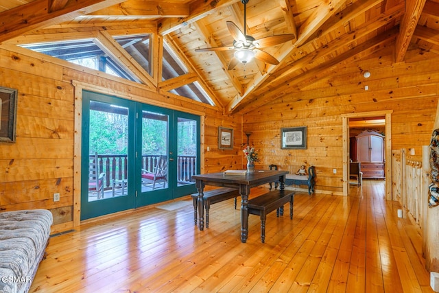 dining space with light wood-type flooring, wood walls, beamed ceiling, and ceiling fan