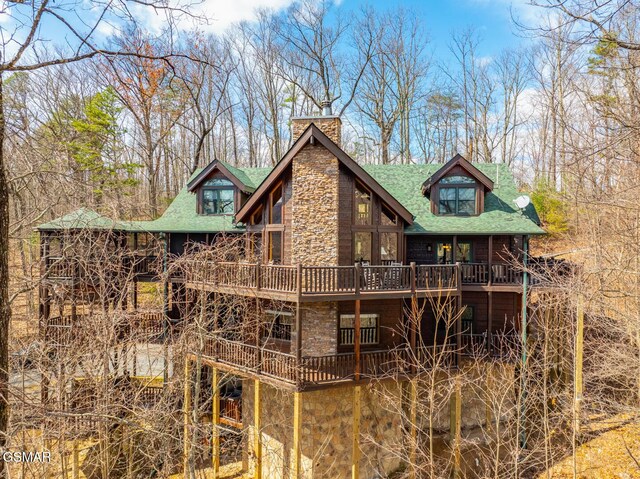 rear view of house featuring stone siding, a shingled roof, a chimney, and a wooden deck