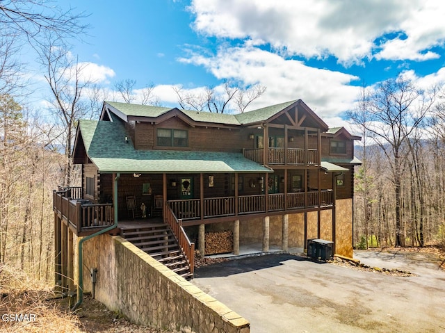 log-style house with aphalt driveway, a balcony, covered porch, a shingled roof, and stairs