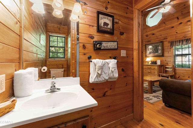 bathroom with wooden walls, wood finished floors, ceiling fan, and vanity