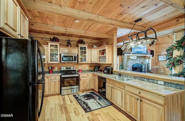 kitchen with black appliances, a sink, light wood finished floors, wooden ceiling with exposed beams, and wood walls