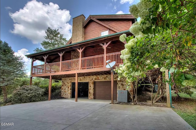 view of front of property with driveway, an attached garage, a chimney, stone siding, and central AC unit