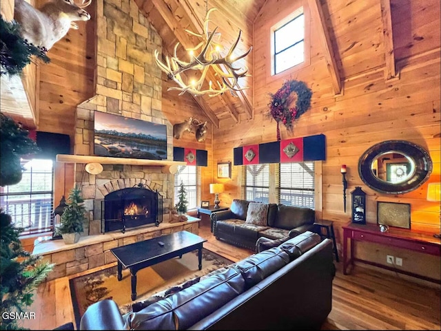 living room with high vaulted ceiling, wood finished floors, a chandelier, a stone fireplace, and wood walls