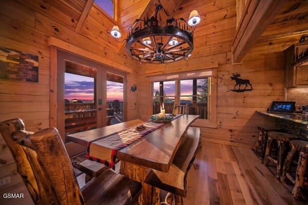 dining area featuring wooden walls, a chandelier, french doors, and wood finished floors