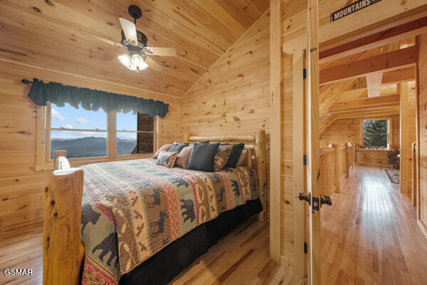bedroom with wooden walls, vaulted ceiling, and wood finished floors