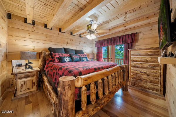 bedroom featuring beamed ceiling, wood ceiling, wood walls, and light wood-type flooring