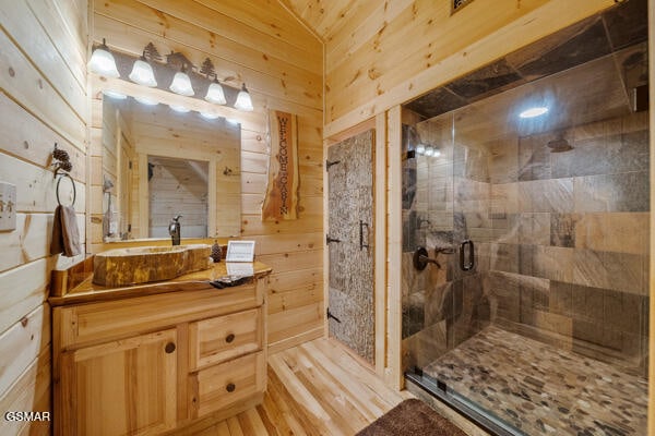 bathroom with vanity, a stall shower, wood walls, and wood finished floors