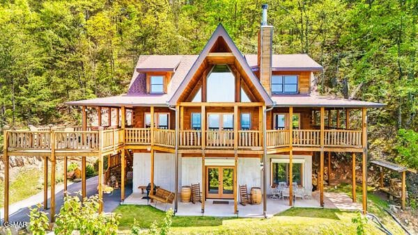 back of house with a wooden deck, french doors, a chimney, a patio area, and a view of trees