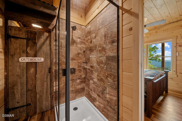 full bathroom with wood finished floors, wooden walls, and a shower stall