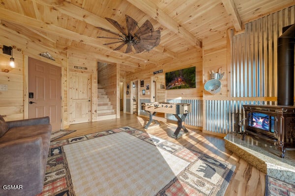 living room featuring a wood stove, wood finished floors, wood walls, and beamed ceiling