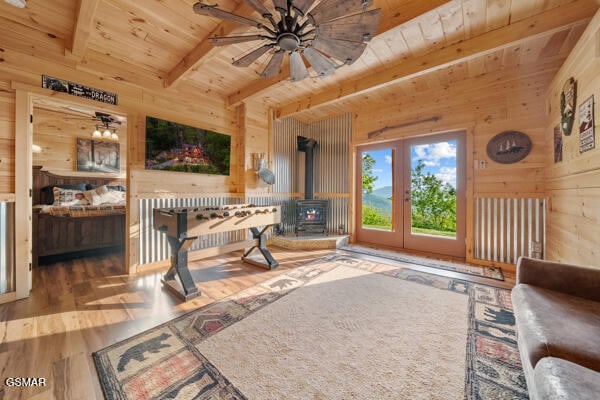 living room with a wood stove, beamed ceiling, ceiling fan, wooden walls, and wooden ceiling