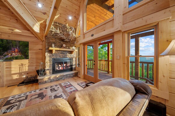 living area featuring french doors, a stone fireplace, beam ceiling, wood finished floors, and high vaulted ceiling