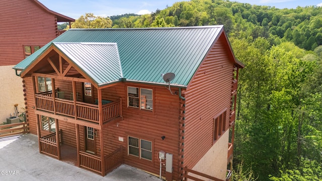 rear view of house with metal roof, log siding, central air condition unit, a view of trees, and a balcony