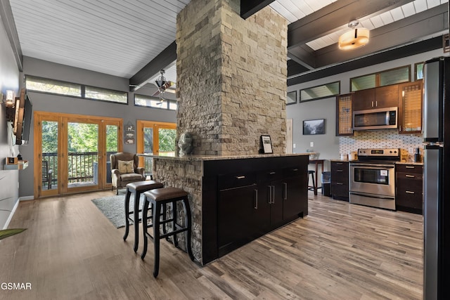 kitchen featuring beam ceiling, a breakfast bar, decorative backsplash, and appliances with stainless steel finishes