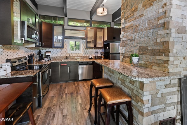 kitchen featuring a kitchen bar, appliances with stainless steel finishes, dark hardwood / wood-style flooring, stone counters, and beamed ceiling