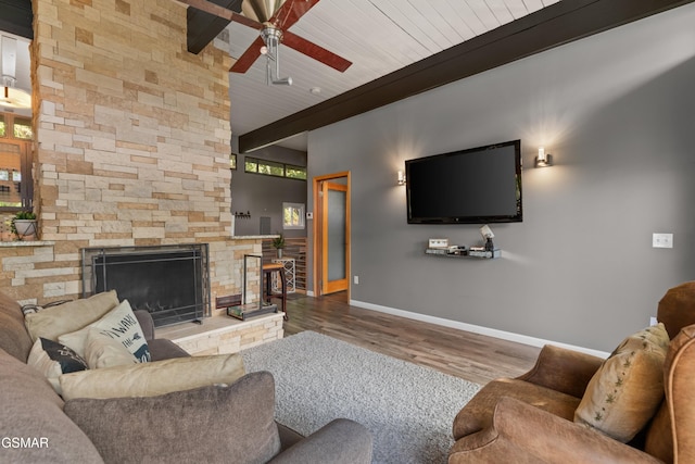 living room with wood ceiling, ceiling fan, wood-type flooring, a stone fireplace, and beamed ceiling