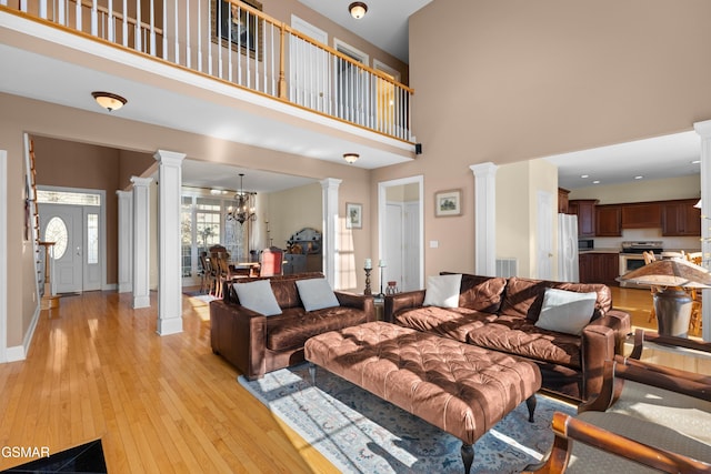 living room featuring a high ceiling, light wood-type flooring, decorative columns, and a notable chandelier