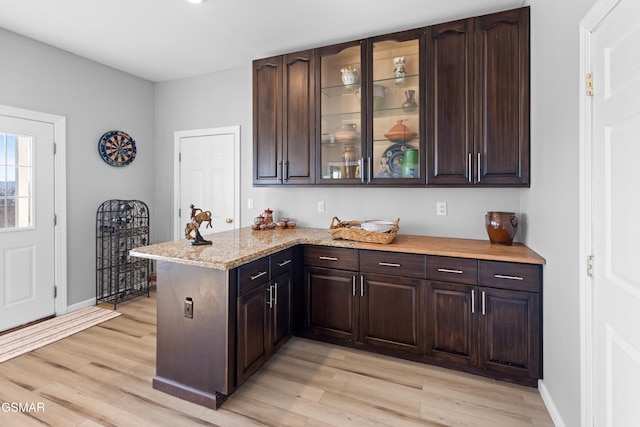 kitchen featuring kitchen peninsula, dark brown cabinets, light wood-type flooring, and light stone counters