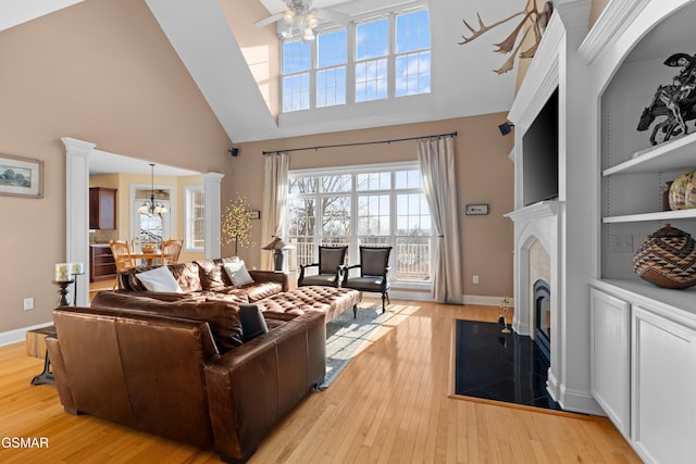 living room with ornate columns, a premium fireplace, light hardwood / wood-style flooring, a towering ceiling, and ceiling fan with notable chandelier