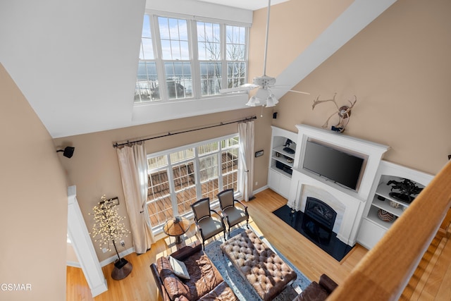 living room with ceiling fan, light wood-type flooring, and a towering ceiling