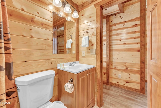half bathroom with wood walls, vanity, toilet, and wood finished floors
