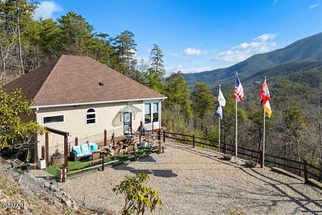 rear view of house with fence, a mountain view, a forest view, and a shingled roof