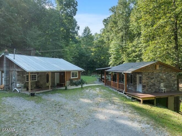 view of front of home featuring metal roof, covered porch, stone siding, driveway, and a forest view