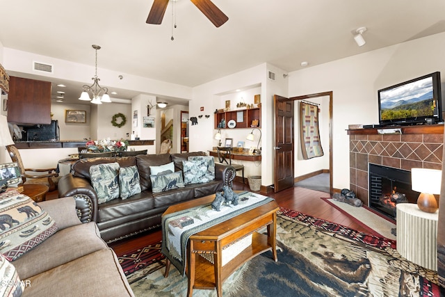 living area with visible vents, ceiling fan with notable chandelier, wood finished floors, and a tile fireplace