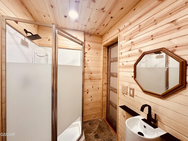 bathroom with a shower with shower door, wood ceiling, sink, and wooden walls