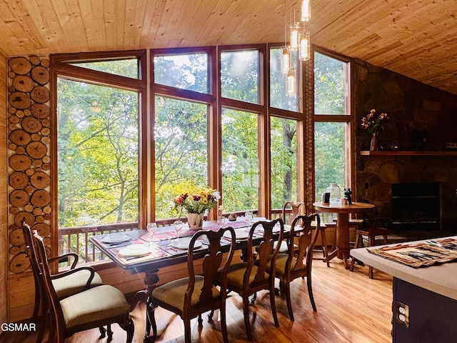 dining room featuring wooden ceiling, an inviting chandelier, a stone fireplace, light hardwood / wood-style floors, and vaulted ceiling